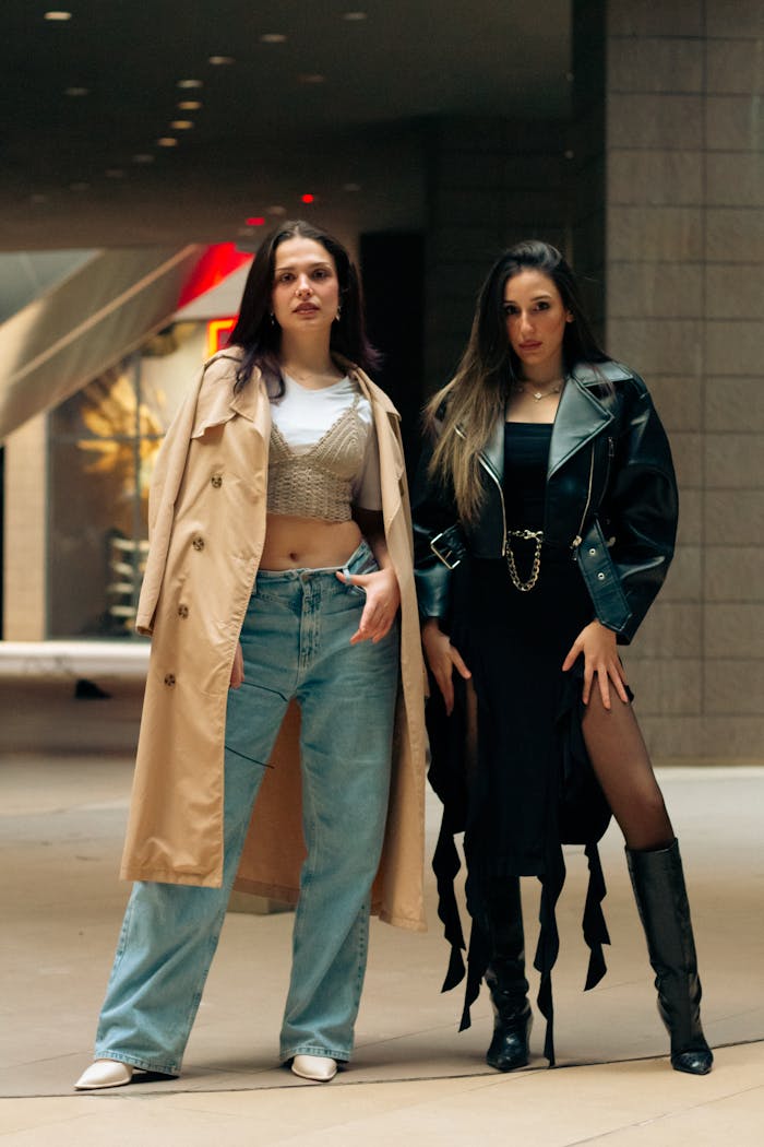 Two stylish women showcase urban fashion trends in a modern city environment.